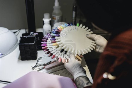 Foto de Una manicurista sosteniendo una paleta de colores para uñas en su salón de manicura - Imagen libre de derechos