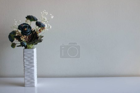 Photo for Home decoration in the form of a vase with artificial flowers. Bouquet of blue roses and a branch of white flowers look aesthetically pleasing on a neutral background - Royalty Free Image