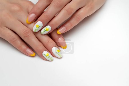 Téléchargez les photos : Manucure française jaune et blanche avec des fleurs peintes sur de longs ongles ovales en gros plan sur le côté gauche sur un fond blanc - en image libre de droit