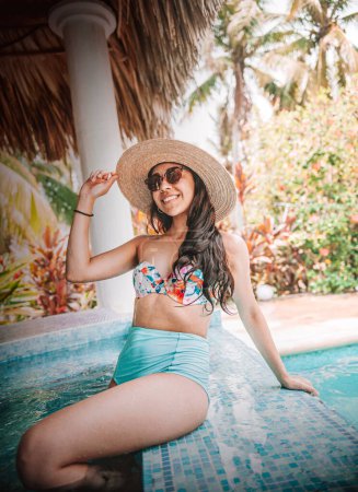Foto de Mujer latina en bikini sonriendo con sombrero y gafas en piscina - Imagen libre de derechos