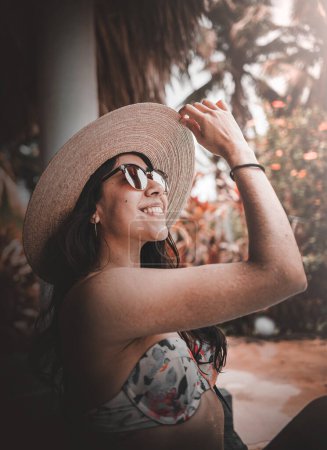 Foto de Mujer en bikini sonriendo con gafas y sombrero, pelo suelto y mirando al cielo - Imagen libre de derechos