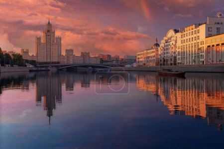 Foto de Serena escena al atardecer sobre un río tranquilo en Moscú, Rusia, con el rascacielos y paisaje urbano de las Siete Hermanas bañado en tonos de atardecer, reflejado perfectamente para un ambiente tranquilo. - Imagen libre de derechos