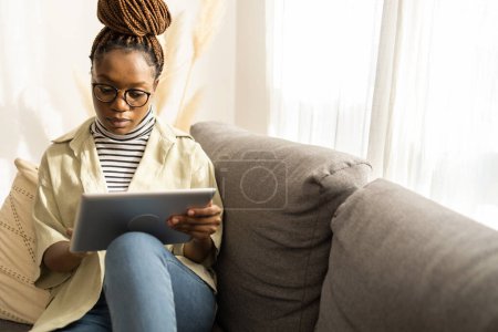 Foto de Joven mujer afroamericana usando tableta digital en casa . - Imagen libre de derechos
