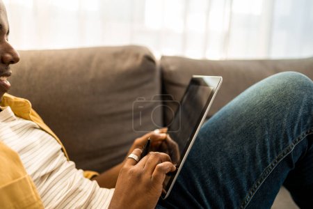 Téléchargez les photos : Gros plan de Jeune Afro-Américain utilisant une tablette numérique à la maison. - en image libre de droit
