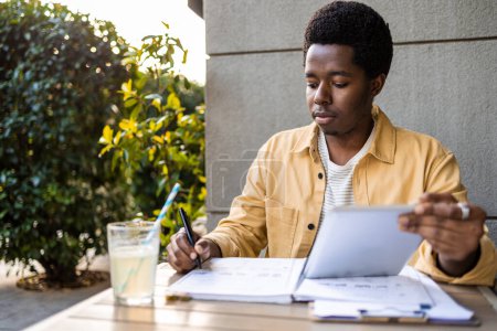 Photo for Young African American man having a video call. He is talking from a bar and writing down the while studying online course - Royalty Free Image