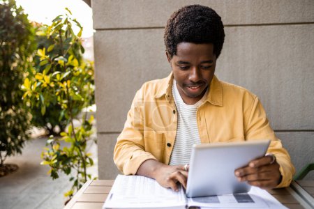 Photo for Front view of young African American man holding digital tablet. He is studying online course. - Royalty Free Image
