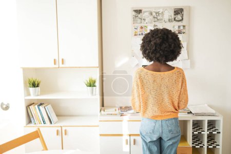 Foto de Vista trasera de una joven freelancer negra irreconocible parada frente a un tablón de anuncios en la oficina en casa - Imagen libre de derechos