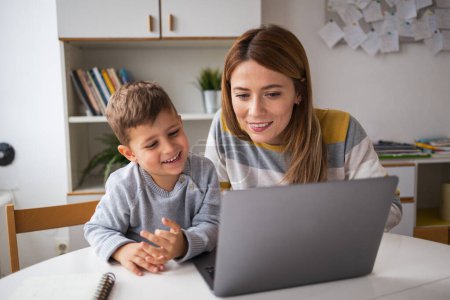 Photo for Smiling young female freelancer taking care of son while working on laptop at desk at home - Royalty Free Image
