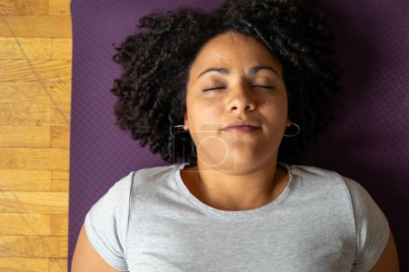 Téléchargez les photos : Directement au-dessus du plan de la jeune femme latine détendue couchée sur un tapis de yoga avec les yeux fermés à la maison - en image libre de droit