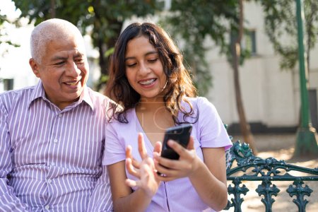 Téléchargez les photos : Grand-père et petite-fille joyeux s'amuser avec les médias sociaux sur le téléphone mobile au parc. Photo de haute qualité - en image libre de droit