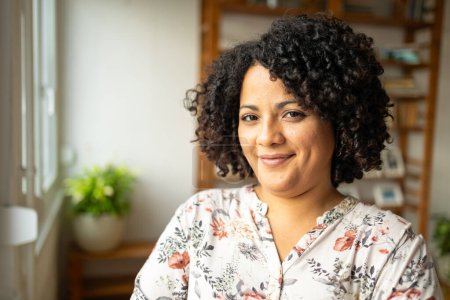 Téléchargez les photos : Portrait de jeune femme latine confiante avec une coiffure afro souriante au bureau à la maison - en image libre de droit