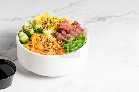 Tuna, carrot, cucumber and vegetable poke served in a white bowl on a marble table. High quality photo