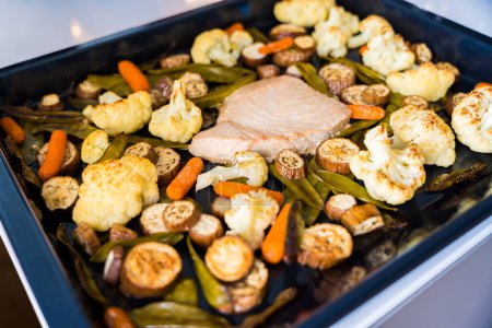 Baked tuna fillet on a baking sheet with baked vegetables. Eggplant, cauliflower, baby carrots, pea pods. High quality photo