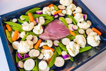 Fresh tuna fillet on a baking sheet with fresh vegetables. Eggplant, cauliflower, baby carrots, pea pods. High quality photo