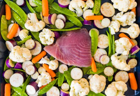 Fresh tuna fillet on a baking sheet with fresh vegetables. Eggplant, cauliflower, baby carrots, pea pods. High quality photo