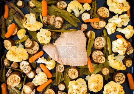 Baked tuna fillet on a baking sheet with baked vegetables. Eggplant, cauliflower, baby carrots, pea pods. High quality photo