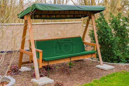 Wooden garden swing with a green mattress and a long seat under the roof. High quality photo
