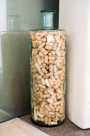 A large transparent decorative bottle filled with a collection of wine corks. Wine collector decor. High quality photo