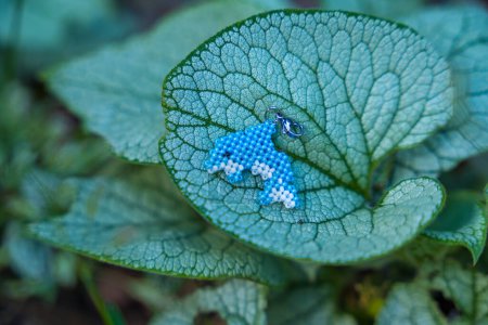 A beaded dolphin keychain is on a large live plant leaf in nature. Handcrafted concept. High quality photo