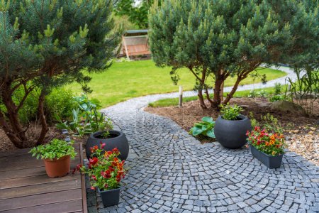 Serene garden path with vibrant potted flowers and lush greenery and fir trees on a sunny day. High quality photo