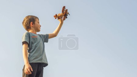 Foto de Niño feliz jugando con juguete avión de madera contra el fondo del cielo. Concepto de educación, futuro, negocios, internacional y viajes - Imagen libre de derechos