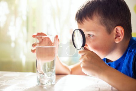 Téléchargez les photos : L'enfant garçon regardant l'eau dans un verre à travers la loupe. Concept de contrôle qualité de l'eau. - en image libre de droit