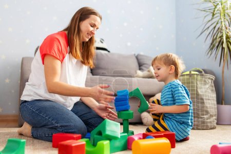 Photo for Cute little kid and child development specialist attractive young woman playing together with colorful blocks, sitting on the floor. - Royalty Free Image