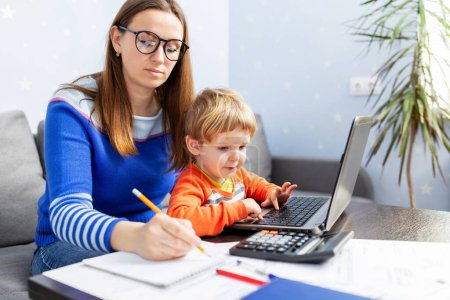 Photo for Young woman working at home with a laptop with a child on her lap. Home office with kids. Mother is working from home - Royalty Free Image