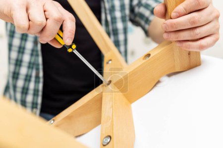 Photo for Self-assembly furniture concept. The young man himself assembling chairs. He uses tools for furniture - Royalty Free Image