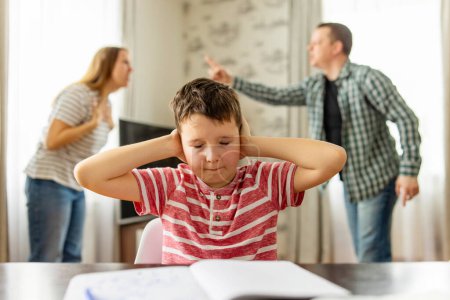 Téléchargez les photos : Un enfant triste se couvre les oreilles avec ses mains lors d'une dispute entre ses parents. Conflits familiaux ou impact du divorce sur le développement de l'enfant - en image libre de droit