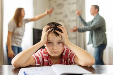 Téléchargez les photos : Un fils se sent frustré pendant que ses parents se battent en arrière-plan. Conflits familiaux ou impact du divorce sur le développement de l'enfant - en image libre de droit