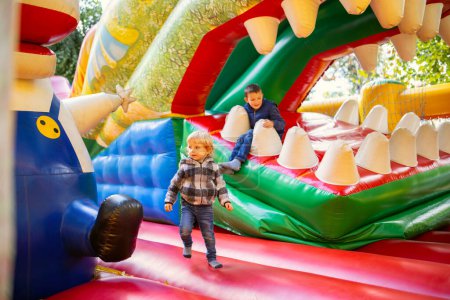 Téléchargez les photos : Enfants heureux s'amusant sur l'aire de jeux gonflable colorée d'attraction. Les enfants s'amusent et roulent sur l'aire de jeux extérieure. - en image libre de droit