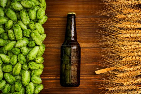 Eine Flasche Bier auf einem hölzernen Hintergrund mit grünen Hopfenzapfen und goldenen Weizenähren, Craft-Beer-Attrappen