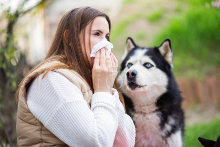 Una mujer estornuda y se sopla la nariz en una servilleta sufre de alergia a la piel de las mascotas. Concepto de alergias a animales domésticos