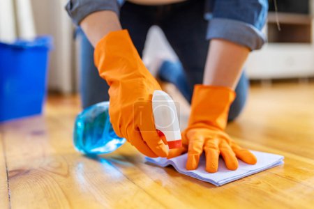 Photo for Young woman in rubber gloves wiping up dust with spray and rag while cleaning the floor of the house - Royalty Free Image