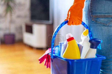 Foto de Mujer en guantes de goma con cubo de suministros de limpieza listo para limpiar su apartamento. Ama de casa tiene muchas tareas domésticas, trabajo doméstico y servicio de limpieza profesional. Baja profundidad de campo - Imagen libre de derechos