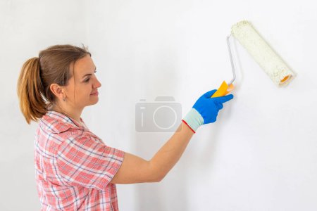 Photo for Happy woman with roller painting wall in her new apartment. Renovation, redecoration and repair concept - Royalty Free Image
