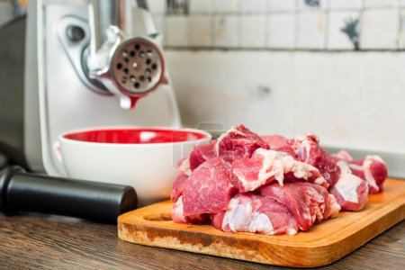 Meat grinder with fresh meat on a cutting board in kitchen interior. Machine for grinding meat into minced meat.