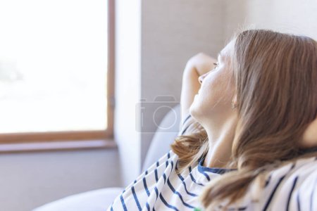 Photo for A peaceful scene of a woman reclining comfortably by a window, basking in the warm, natural sunlight. - Royalty Free Image