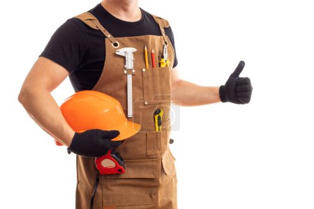 Ein professioneller Bauarbeiter in brauner Schürze hält einen Schutzhelm in der Hand, während er vor weißem Hintergrund gestikuliert.