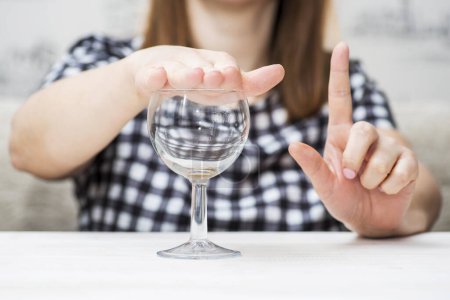 A womans hand is shown gesturing no to a glass of water, symbolizing alcohol refusal or a commitment to sobriety.