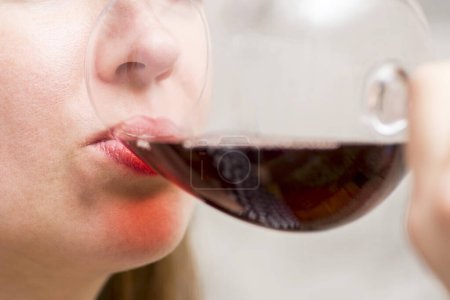 Macro shot of a woman tasting red wine, focusing on her lips and the glass edge, highlighting the sensory experience.