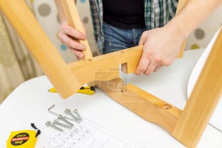 Großaufnahme von Händen, die Holzmöbelteile mit Werkzeug und Montageanleitung auf einem Tisch zusammensetzen.