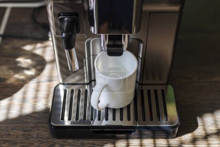 A sleek espresso machine fills a white mug with fresh coffee in a home setting.