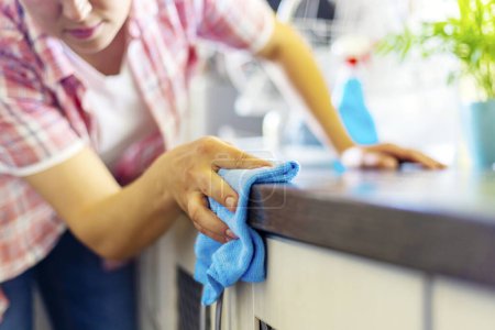 Frau putzt Küchentheke mit blauem Tuch.