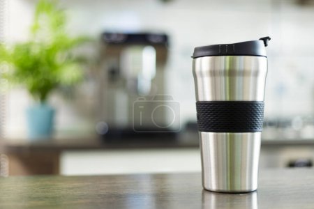 Photo for A sleek stainless steel travel mug with a black grip stands ready on a kitchen counter, showcasing the modern on-the-go lifestyle. - Royalty Free Image