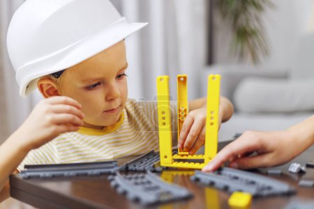 A focused child wearing a hard hat plays with a construction toy set indoors.