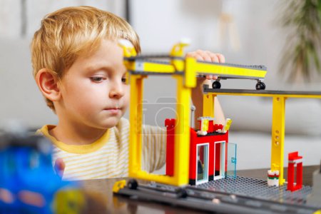 Ein kleiner Junge ist sehr darauf fokussiert, eine Struktur mit einem Spielzeugbaukasten zu bauen, was seine Konzentration und Kreativität unterstreicht..