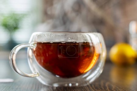 Nahaufnahme einer heißen, dampfenden Tasse Tee auf einem Holztisch mit verschwommenem Hintergrund.