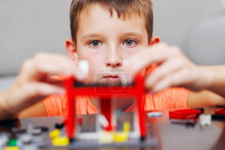 Close-up of a young boy deeply focused while assembling a red toy building set, showcasing his concentration and dexterity.